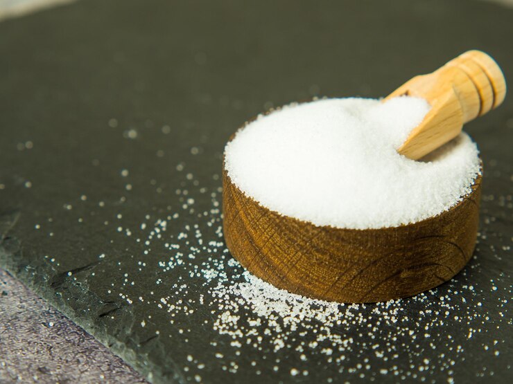 White salt on a dark concrete background in a wooden bowl and spoon