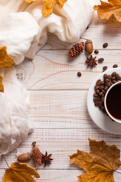 Белый шарф, чашка кофе с разбросанными кофейными зернами, сухие желтые листья на деревянном столе. Осеннее настроение, copyspace.