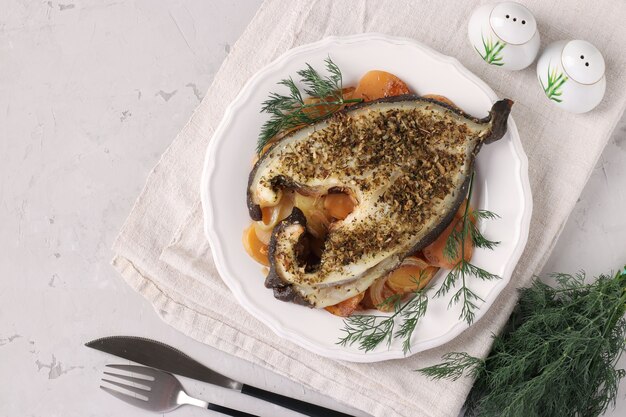 Фото Стейк из белой морской рыбы с луком, морковью и укропом на белой тарелке. вид сверху