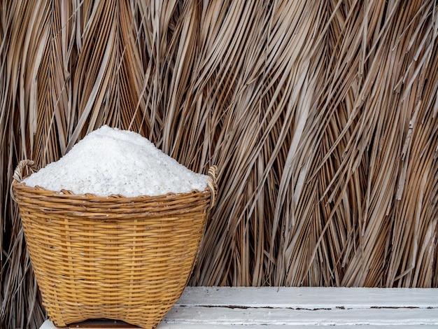 Photo white sea salt in yellow basket on dried tropical palm leaves background