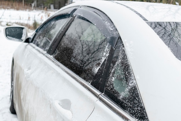 A white sedan car automobile on winter countryside road covered in snow ice closeup reflection