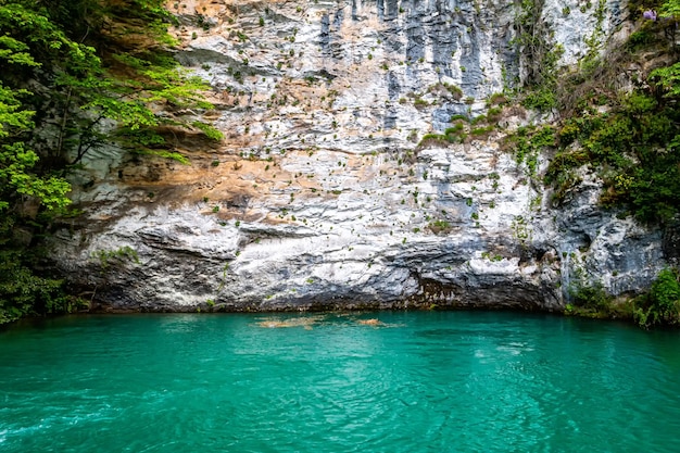 White sheer cliff covered with greenery and a blue lake