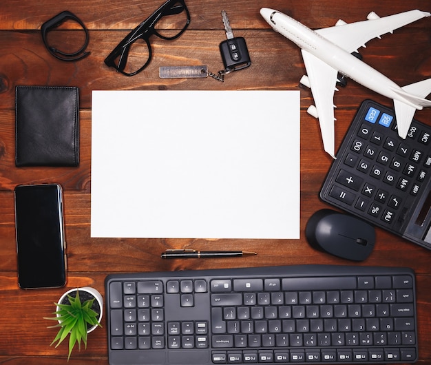 Foglio bianco sul tavolo della scrivania in legno scuro con molte forniture. vista dall'alto, piatto. desktop da ufficio moderno con tastiera, mouse e piccola pianta verde. sfondo di affari con accessori per computer