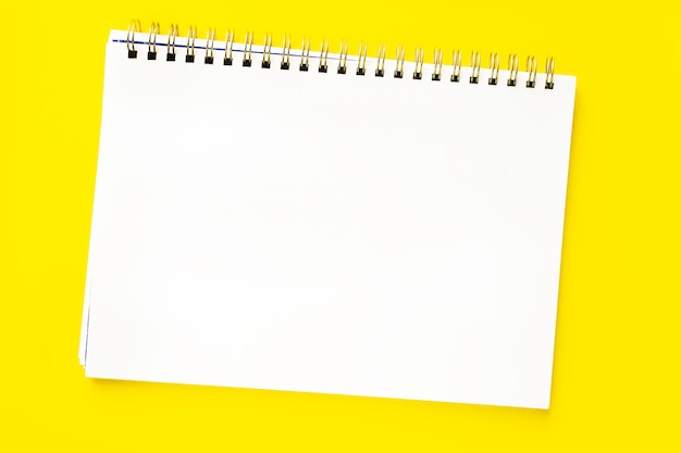 White sheet of an open notebook with a spiral on a yellow background. Copy space or space for text