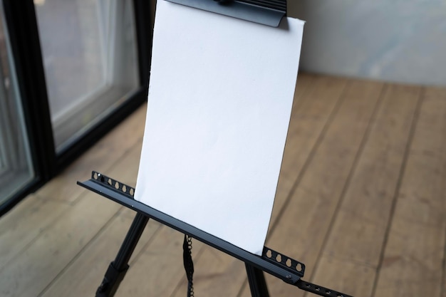 Foto un foglio di carta bianco su un cavalletto nero in una stanza con pareti bianche e pavimento in legno