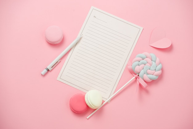Un foglio di carta bianco, macaron, caramelle su sfondo rosa
