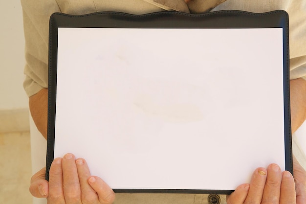 A white sheet  of a paper  with free space for a text in the hands of senior woman