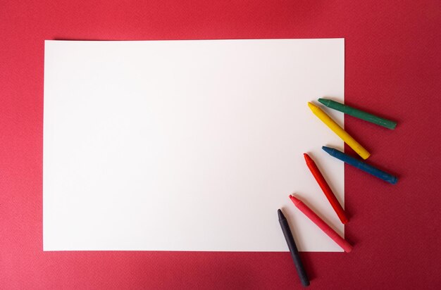 White sheet of paper with wax crayons on a magentacolored background