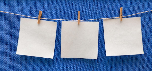 White sheets of paper hanging isolated on a blue beige board on clothespins free space mockup