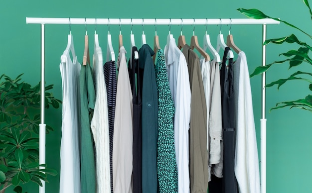 White shelf with a lot of clothes on the green background with green big plant.