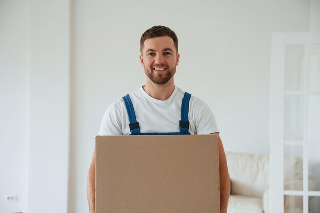 Фото Белая рубашка и синяя униформа с коробкой в руках переезжающий сотрудник в комнате