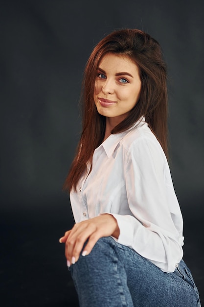 In white shirt and blue jeans Young beautiful woman is posing for the camera in the studio