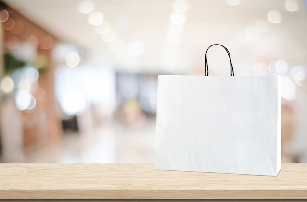 White shopping bag on wooden table over blurred store background, business, template, product display montage background