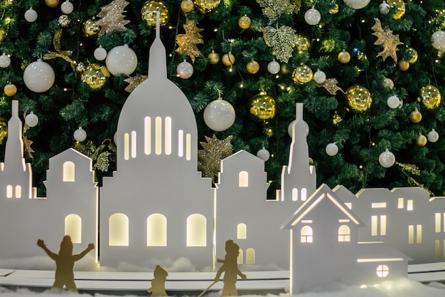 White silhouettes of houses and children, against background of decorated Christmas tree