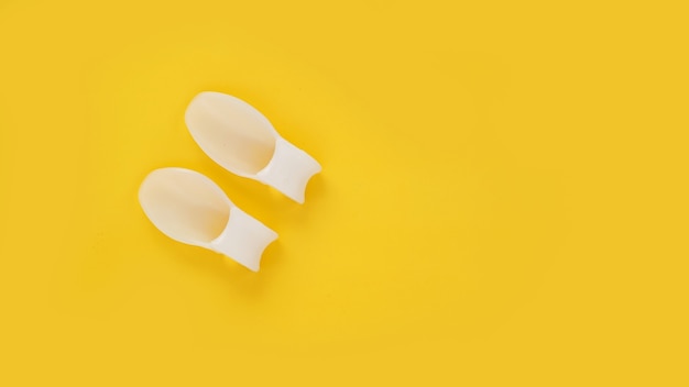 Белый силиконовый разделитель пальцев на желтом фоне. Профилактика и лечение вальгусной деформации большого пальца стопы