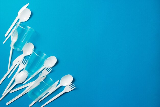 White single-use plastic knives, spoons, forks on a blue background. 