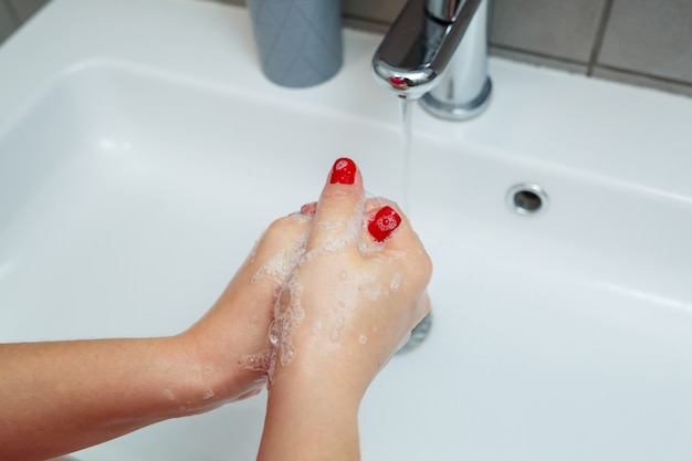 White sink with a silver faucet in the bathroom. Gray can with liquid soap for hands. Turning on the tap water, personal hand hygiene. Hand washing under running water