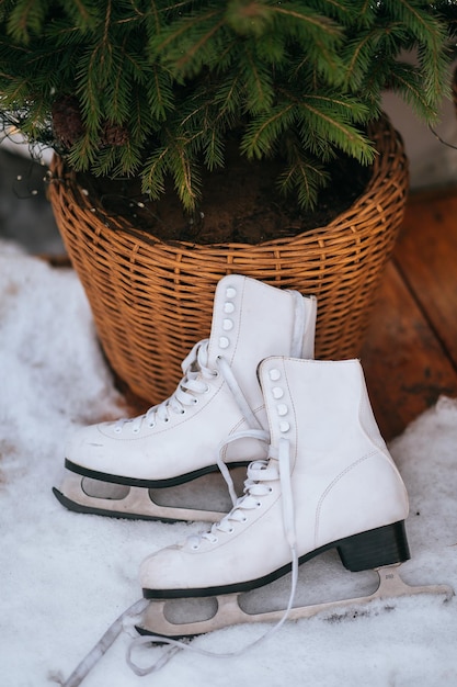 Photo white skates on snow leaning on wicker basket with christmas tree inside winter leisure activities