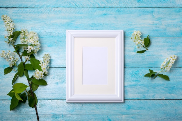 White small frame mockup with blooming bird cherry branch on the blue wooden table Empty frame mock up for presentation artwork Template framing for modern art