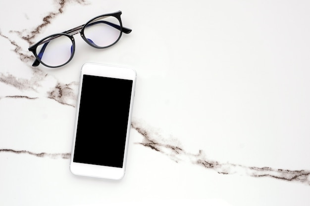 White smart phone with blank screen and eyeglasses on white marble