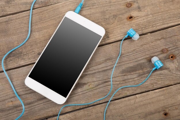 White smartphone with headphones on the old wooden board