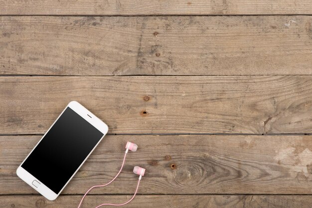 White smartphone with headphones on the old wooden board