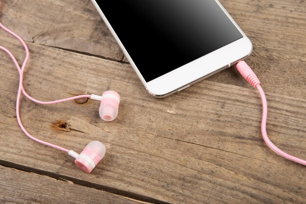 White smartphone with headphones on the old wooden board