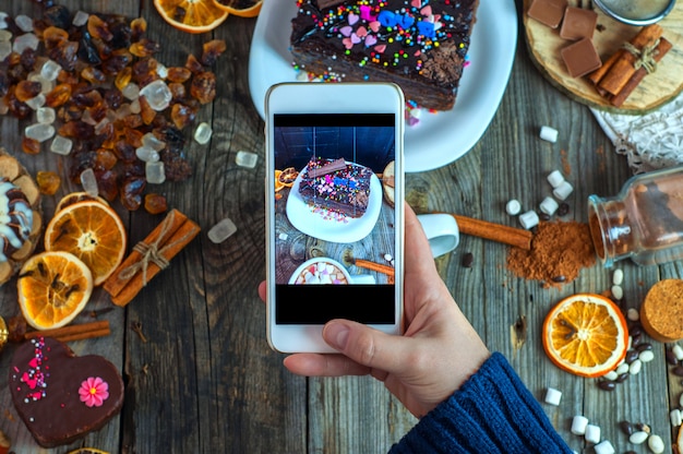 White smartphone in a woman's hand takes a piece of cake and sweets