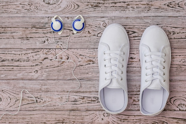 Foto scarpe da ginnastica bianche e cuffie blu sul pavimento di legno.