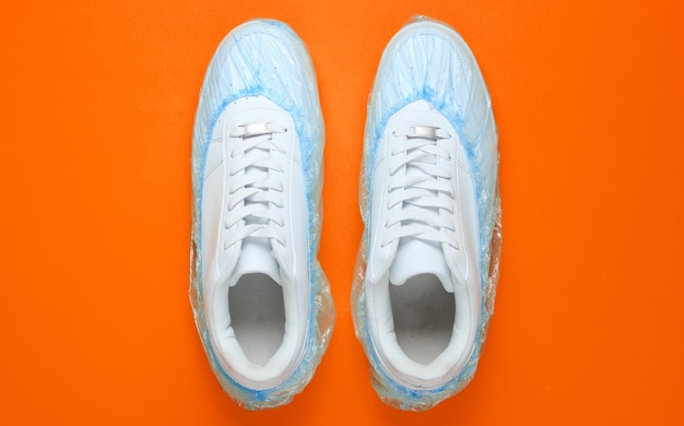 White sneakers in boot covers on orange background. Top view. Minimalism