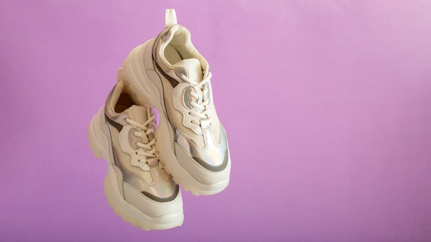 Le scarpe da ginnastica bianche volano sulla parete viola. scarpe femminili in pelle bianca su sfondo viola. coppia di eleganti sneakers urbane. comode scarpe da donna hipster di abbigliamento sportivo. banner web lungo con spazio di copia.