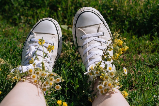 White sneakers on girl legs on grass during sunny summer day