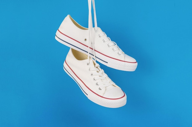 White sneakers hanging on laces on a light blue background