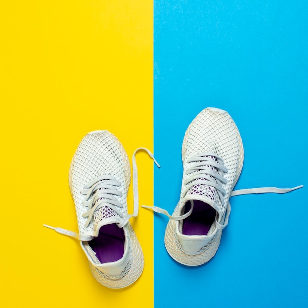 White sneakers for running on abstract yellow and blue surface. Concept of running, training, sport. Square. Flat lay, top view