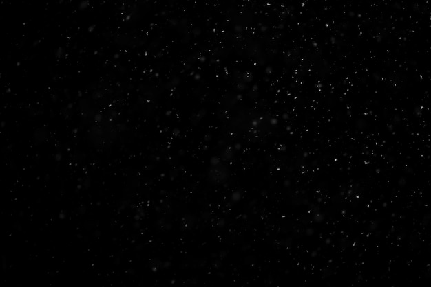 White snow falling in black night sky in the dark