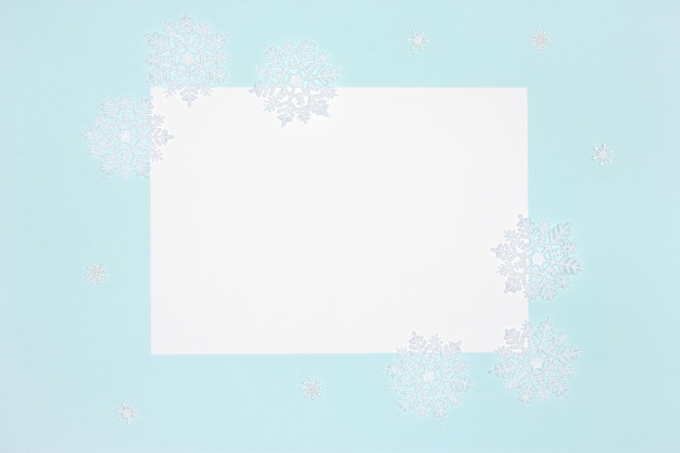 White snowflake decorations with blank paper on blue background. Winter card. Copy space