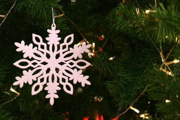 White snowflake ornament hanging on sparkling Christmas tree