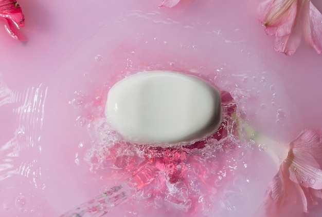 Foto saponetta bianca in spruzzi d'acqua rosa con il concetto di cura del corpo dei fiori