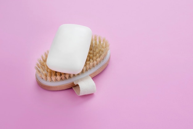 White soap bar on wooden brush against pink wall. Body and beauty care concept