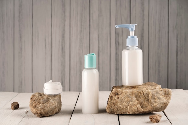 White soap and cream containers on natural stones and wooden background