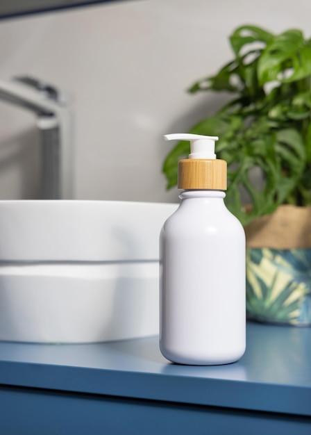 Foto dispensatore di sapone bianco vicino al lavandino e monstera verde in bagno blu e grigio close up mockup