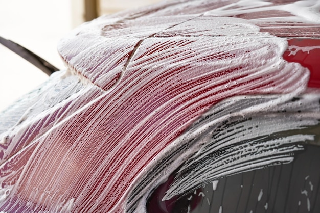 White soap and foam strokes on red plates of car washed in self serve carwash, closeup detail