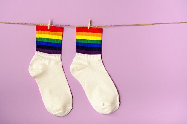 White socks with colored rainbow stripes suspended on chips on pink background, idea for lgbtq gift, copy space, symbol of lgbt