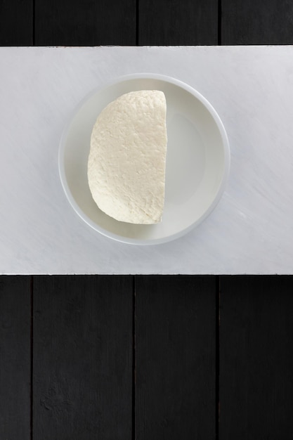 White soft brynza or feta cheese on a white plate on a white background Vegetarian food concept Closeup View from above