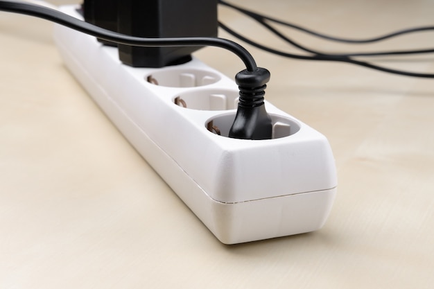 Photo a white splitter socket with plugs from different devices included in it lies on the light surface of the diagonal.