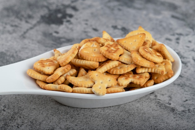 White spoon full of crispy crackers placed on a stone background . 