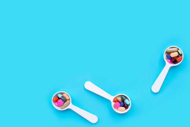 White spoon with colorful medicine pills, tablets and capsules on blue background.