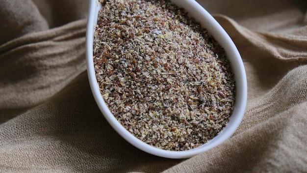 Photo white spoon with ground flax on a brown cloth background