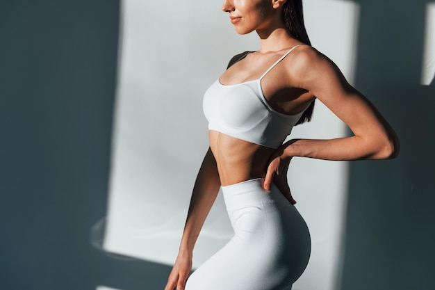 In white sportive clothes Young caucasian woman with slim body shape is indoors at daytime
