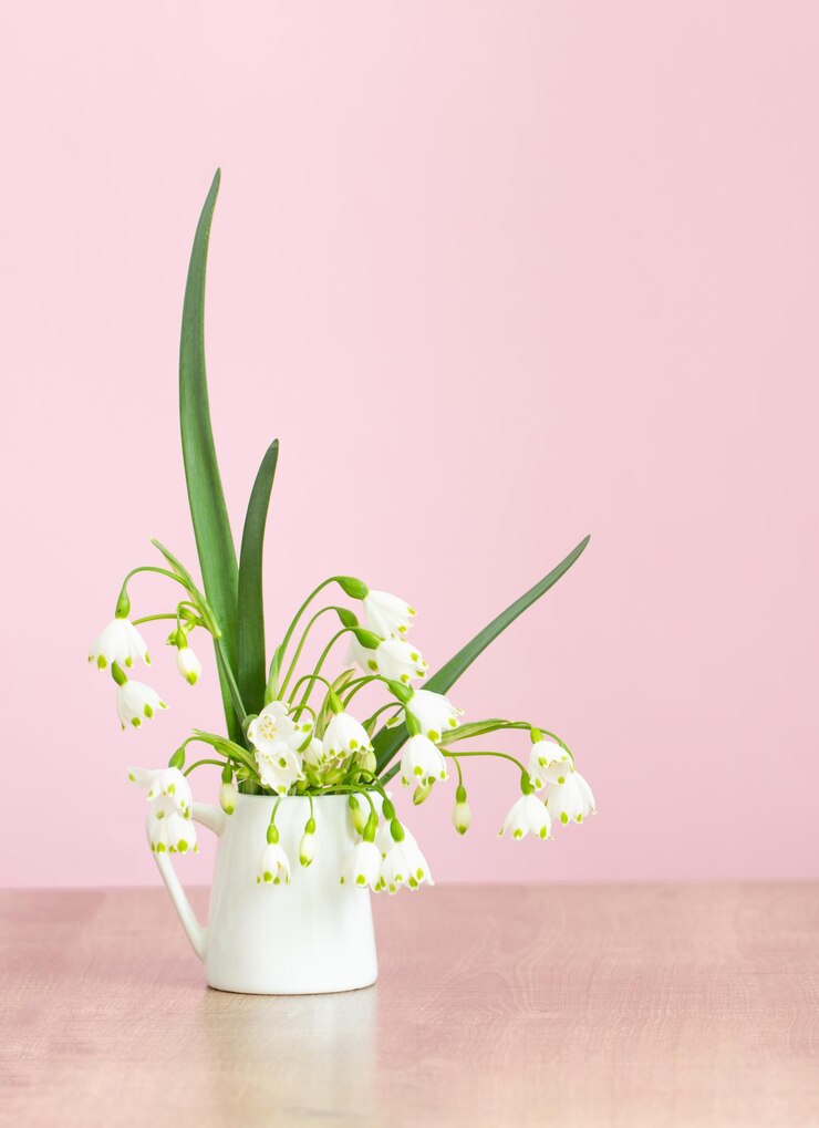 White spring flowers in jug on pink background
